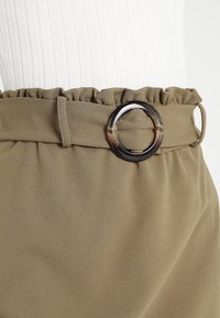 Gonna di tessuto verde con una cintura arricciata e una grande fibbia per cintura in tartaruga circolare. Tessuto liscio e vestibilità sartoriale.