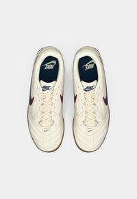 Białe skórzane sneakersy z czerwonymi i niebieskimi akcentami, teksturowaną powierzchnią, sznurowaniem i gumową podeszwą. Logo Nike na języku i bokach.