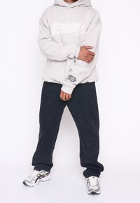 Felpa grigia chiara con logo bianco. Pantaloni neri a gamba dritta. Scarpe da ginnastica argentate con dettagli neri. Outfit semplice e casual.