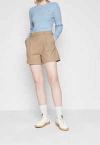 Jasnoniebieski sweter na drutach z prążkowaniem, beżowe szorty z wysokim stanem, białe trampki z beżowymi podeszwami oraz białe skarpetki do kostek. Prosty i nowoczesny styl.