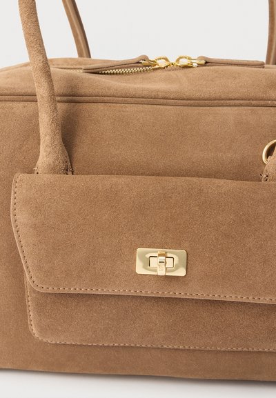 Καφέ τσάντα χειρός από σουέτ με εμπρόσθια τσέπη με καπάκι, χρυσό κούμπωμα τύπου turn-lock, επάνω φερμουάρ με διπλά χρυσά τερματικά και στρογγυλεμένες λαβές.