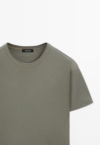 T-shirt en coton vert olive à manches courtes, col rond et détails de couture visibles sur le col et les manches.