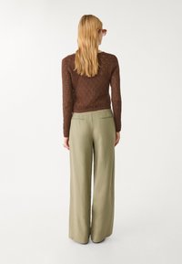 Bruine gebreide top met een ruitenpatroon, gecombineerd met olijfgroene broek met wijde pijpen, voorzien van een gladde textuur en achterzakken.