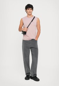 Lyserød ærmeløs t-shirt stylet med grå vidde bukser. En lille sort crossbody-pung hviler på modellens skulder. Sorte sneakers fuldender looket.