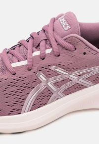 Chaussure de sport violette avec tige en mesh, accents blancs, superpositions texturées et semelle légère. Présente un col rembourré et des lacets.