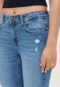 Light blue distressed jeans with a high waist, featuring a button closure, pockets, and subtle fraying on the fabric.
