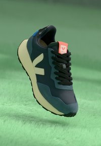 Navy and black sneaker with a textured finish, white sole, and reflective accents. Features a vibrant orange logo on the tongue.