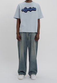 Světle modré tričko s krátkým rukávem a černě vyšitým logem "Lowlights" na přední straně, spárované s volnými džínami v světle modré barvě a bílými teniskami.