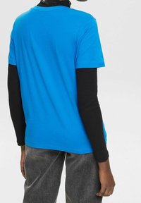 Blå bomulds t-shirt med rund halsudskæring, korte ærmer og en glat tekstur, parret med en sort ribbet langærmet top underneath.