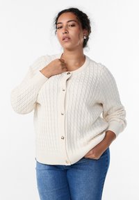 Kreemivärviline heegeldatud kardigan tekstuurse palmikmustriga, millel on ümmargune kaelus ja esiküljel kuldsed nööbid.