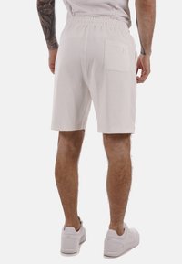 Pantaloni corti bianchi in cotone con vita elasticizzata, una tasca posteriore e un taglio dritto, abbinati a sneaker bianche. Texture liscia.