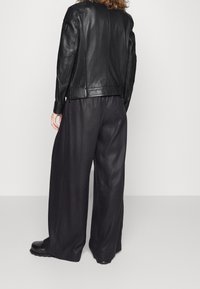 Černá kožená bunda s žebrovanými detaily, v kombinaci s volnými černými kalhotami. Hladká textura a strukturovaný design, minimální kovové doplňky.