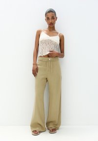 Kanten crop top in ivoor, hooggeplaatste beige wijde broek met een trekkoord en knoopdetail, gedragen met lichte sandalen. Soepele texturen.