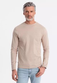 Vaaleahko pitkähihaisessa paidassa on pyöreä kaula-aukko, se on valmistettu pehmeästä puuvillasta ja siinä on slim fit -malli sekä hienovaraisia ompelut yksityiskohtia.