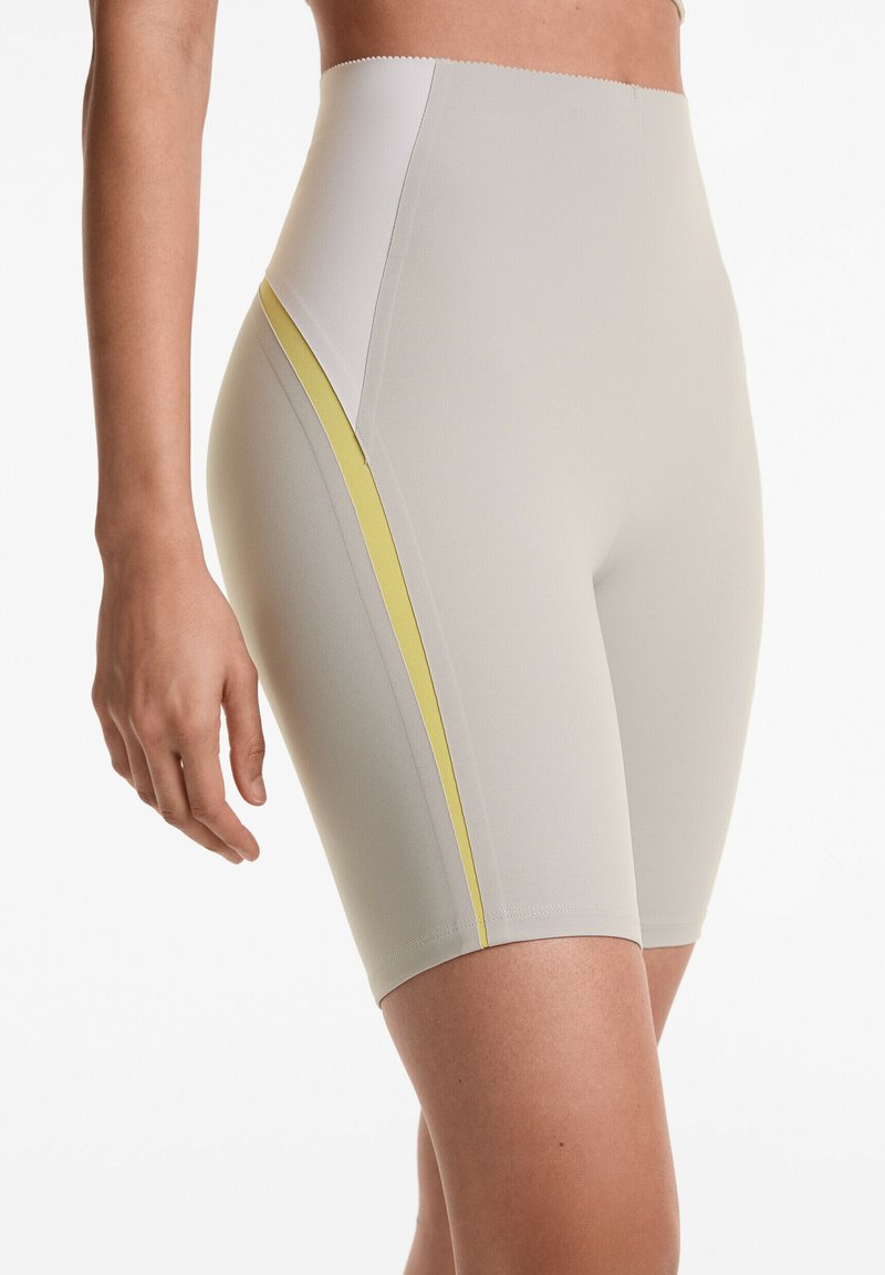 Höga kompressionsshorts i ljusbeige med en kontrasterande gul sidremsa, slät textur och åtsittande design för komfort.