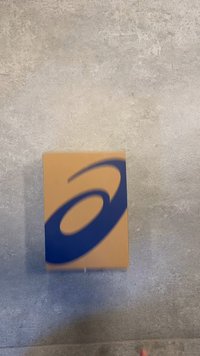 Caja de cartón marrón con un gran logo azul en la parte superior. La caja tiene bordes limpios y una textura suave. Ideal para empaquetar zapatos o ropa.