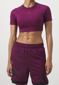 Sportovní postava oblečená v modrém crop topu a odpovídajících sportovních šortkách, stojící na jednotném světlém pozadí.