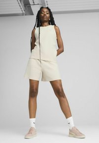 Top sin mangas beige y pantalones cortos de tela texturizada. Combinado con zapatillas rosa claro y calcetines blancos que llevan un logo negro.