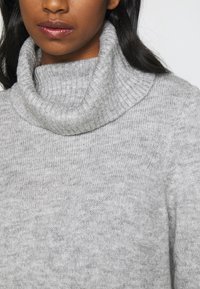 Maglione grigio a maglia con colletto alto e texture morbida, caratterizzato da una vestibilità casual e cuciture minimali.