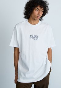 Vit bomullströja med avslappnad passform, med tryckt textdesign "the new originals jazz club" i blått och grått på framsidan.