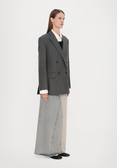 Blazer grigio a doppio petto con rever a punta, abbinato a una lunga gonna in denim bicolore. Scarpe nere e camicia bianca con colletto sotto.