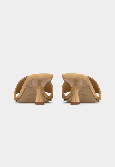 Bézs bőr mamuszmagassarkúk fonott pántokkal, közepes magasságú, kúpos sarkakkal, hátulról fényképezve fehér háttéren.