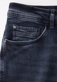 Mörkblå denimjeans i närbild som visar framfickan med liten myntficka och metallnitar.