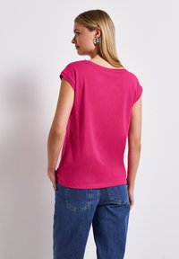 Fuchsie krátký rukáv s uvolněným střihem, kulatým výstřihem a hladkým povrchem. V kombinaci s modrými širokými džíny s zadními kapsami.