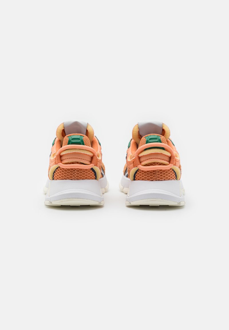 Pomarańczowe sneakersy z siateczki z białymi podeszwami, wyściełanymi kołnierzami pięty i zielonymi akcentami. Charakteryzują się solidną, teksturowaną powierzchnią oraz podwójnym systemem sznurowania.