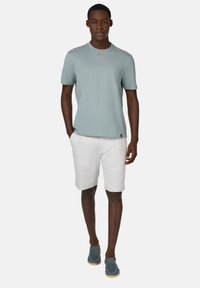 Chemise légère bleu clair à manches courtes, shorts blancs et chaussures en suède gris-bleu. Coupe décontractée, texture lisse et design simple.