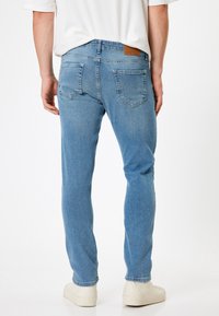 Jeans in denim blu chiaro con taglio dritto, caratterizzati da due tasche posteriori, un'etichetta in pelle sulla vita e una leggera texture sbiadita.