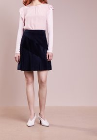 Blouse rose clair avec manches volantées et jupe en velours côtelé bleu marine foncé à panneaux diagonaux. Des chaussures blanches à talons hauts complètent la tenue.