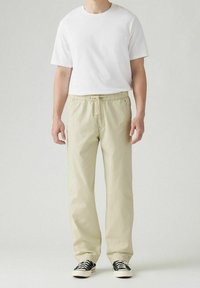Witte t-shirt met korte mouwen gecombineerd met lichtbeige, relaxte broek met elastische tailleband. Zwart-witte sneakers maken de outfit compleet.