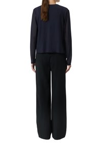 Granatowa bluzka z długim rękawem o luźnym kroju, zestawiona z czarnymi spodniami szerokimi na nogawkach. Gładka struktura materiału z minimalnymi detalami.