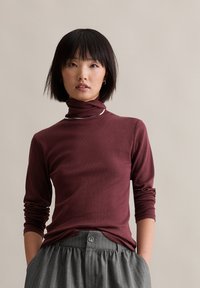 Maroon turtleneck top made of soft fabric, featuring a fitted design and long sleeves, paired with gray pinstriped trousers.