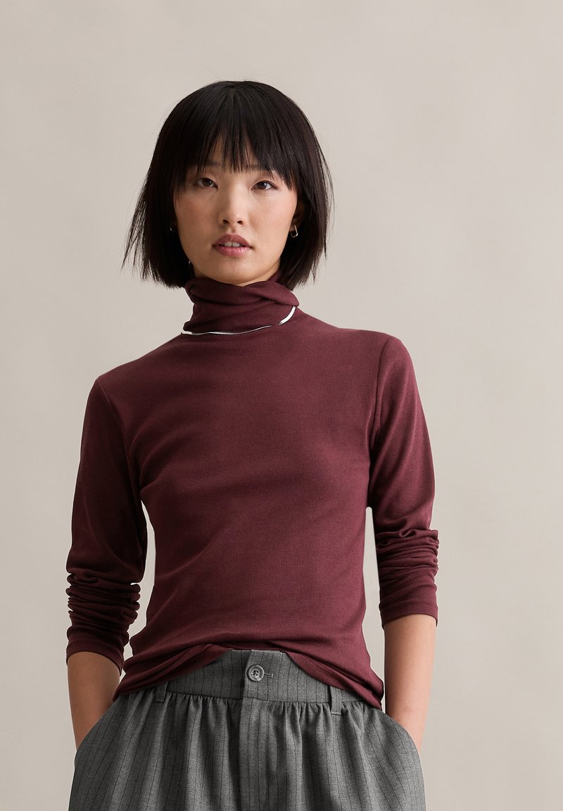 Maroon turtleneck top made of soft fabric, featuring a fitted design and long sleeves, paired with gray pinstriped trousers.