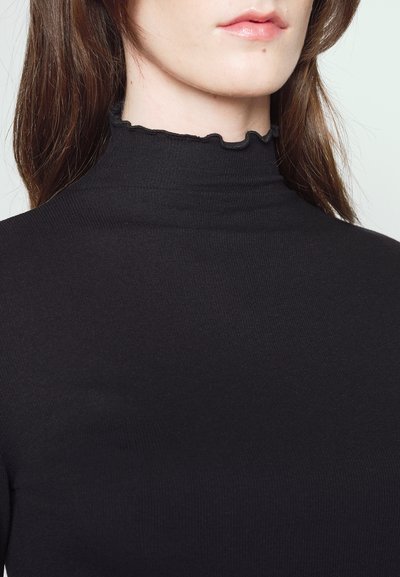 Suéter de cuello alto negro con una textura ribeteada y un detalle de escote con ondas, mostrado desde la clavícula hacia arriba. La tela parece elástica y ajustada.