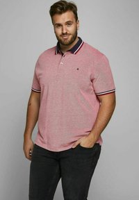 Rood en grijs gestreepte polo met een marineblauwe kraag en een twee-knops sluiting, gemaakt van textuurstof. Draagt men met zwarte jeans.