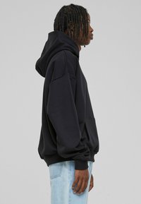 Black oversized hoodie with a kangaroo pocket, hood, and ribbed cuffs. Made of soft fabric, featuring a relaxed fit and minimal design.