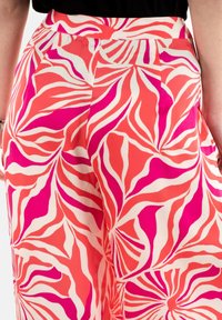 Pantalones rosados y coral con un gran patrón de hojas repetido en blanco y rosa más oscuro. Fabricados en una tela suave con un corte relajado y bolsillos laterales.