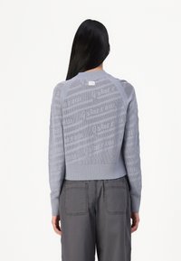 Pull en tricot bleu clair avec un motif texturé et un ourlet côtelé. Manches longues, col rond et une petite étiquette à l'arrière du col.