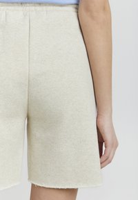 Beige shorts laget av mykt, teksturert stoff, med elastisk midjebånd og rå kanter. Nærbilde av baksiden som viser en avslappet passform.