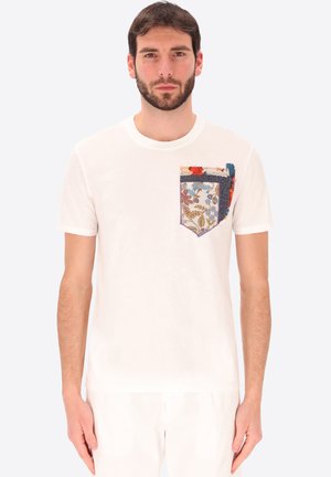 Uomo che indossa una t-shirt bianca tinta unita a maniche corte con una tasca decorativa a fiori multicolore sul petto sinistro.