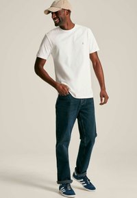 Valge puuvillane T-särk, tume sinine teksapüksa, sinised spordijalatsid valgete triipudega, beež müts. Casual sobivus, lühikesed varrukad, särk on nähtava logoga.