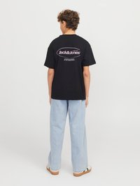 Svart bomulls-T-skjorte med en rund rosa logo på baksiden, kombinert med lyseblå vide jeans og nøytrale sko.