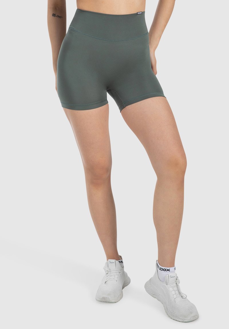 Pantalones cortos deportivos de talle alto en color verde oliva, fabricados con un tejido elástico, que presentan una textura suave y un diseño ajustado. Zapatillas blancas visibles.