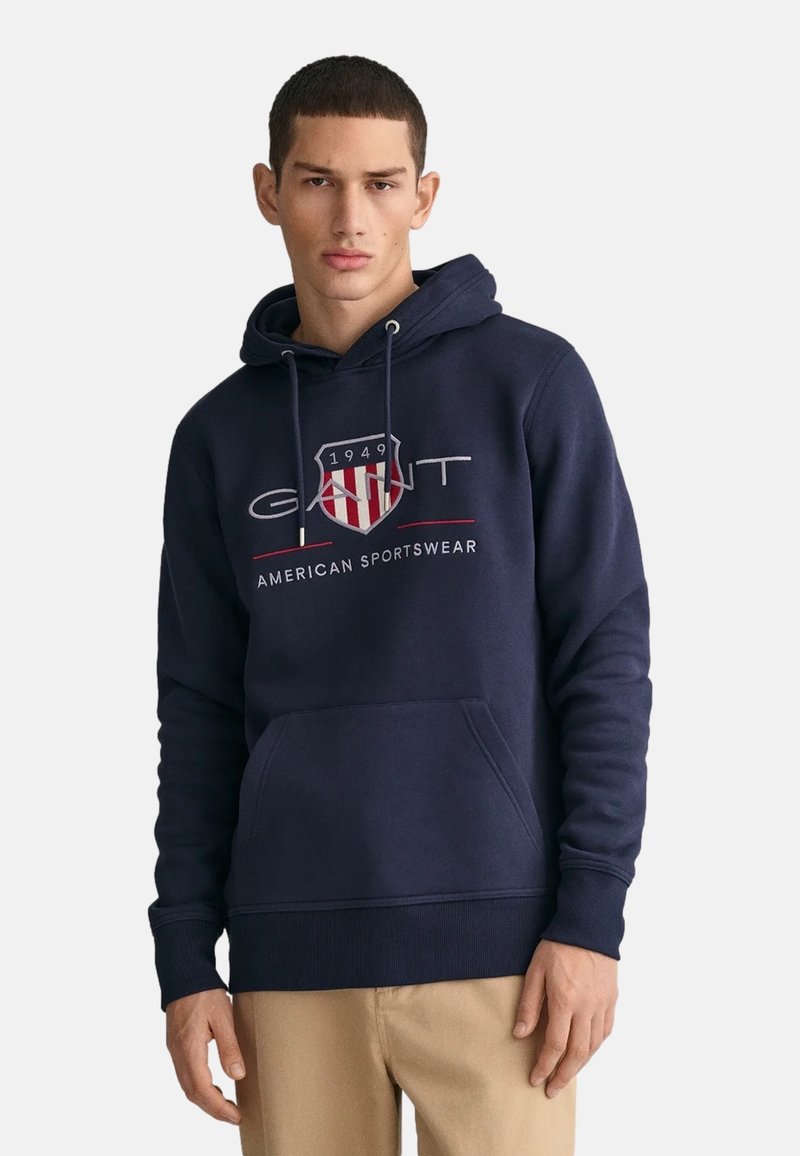 Felpa con cappuccio blu navy realizzata in misto cotone. Presenta una tasca frontale, polsini a coste e un logo grafico con un design a scudo.