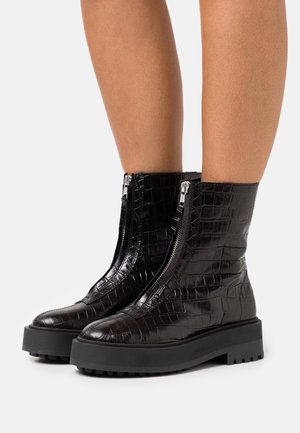 Bottines noires avec une texture crocodile, dotées d'une fermeture éclair à l'avant et d'une semelle noire épaisse avec une bonne adhérence.