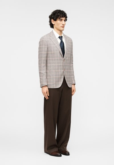 Γκρι σακάκι με καρό μοτίβο και ενδιάμεσους πέτους, συνδυασμένο με σκούρο καφέ παντελόνι. Το ύφασμα έχει υφή και διακριτικό σχέδιο καρό.