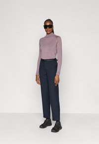Langærmet, tætsiddende lilla rullekravesweater parret med højtaljede, vide marineblå bukser og sorte sneakers. Sorte solbriller.